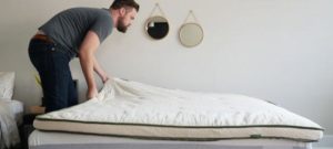 A man places the Avocado topper on a mattress.