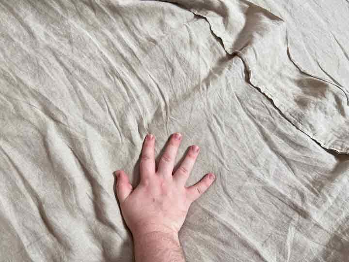 The Best linen Sheets: a hand is moving over a set of beige linen sheets, which are known to have a texture.