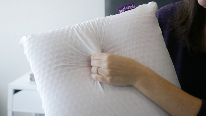 A woman pinches the outer layer of the Purple Harmony Pillow
