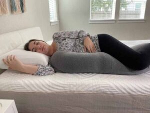 A pregnant woman rests on her side with the Frida Mom pillow