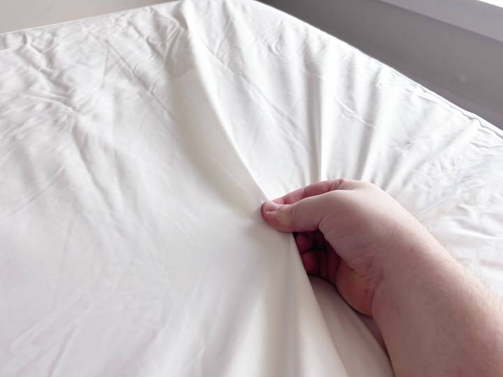 A hand pinches the Nest Bedding mattress protector.