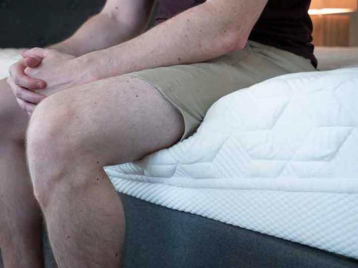A man sits near the edge of an online mattress.