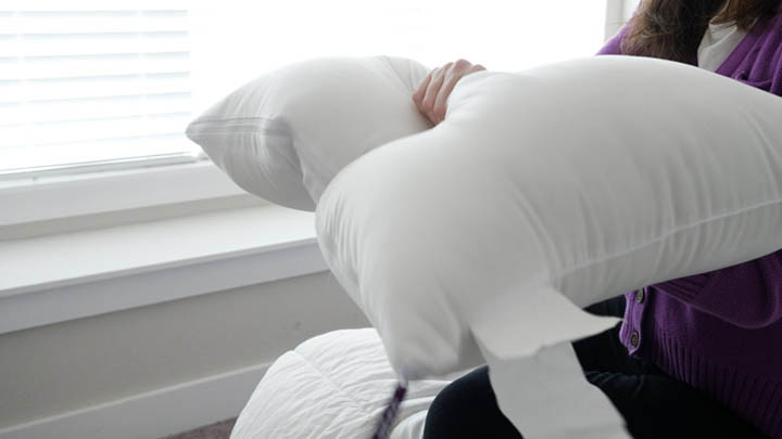 A woman squeezes a pillow, testing out how firm or soft it feels.