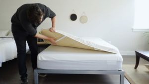 A man attaches the Saatva topper to a mattress.